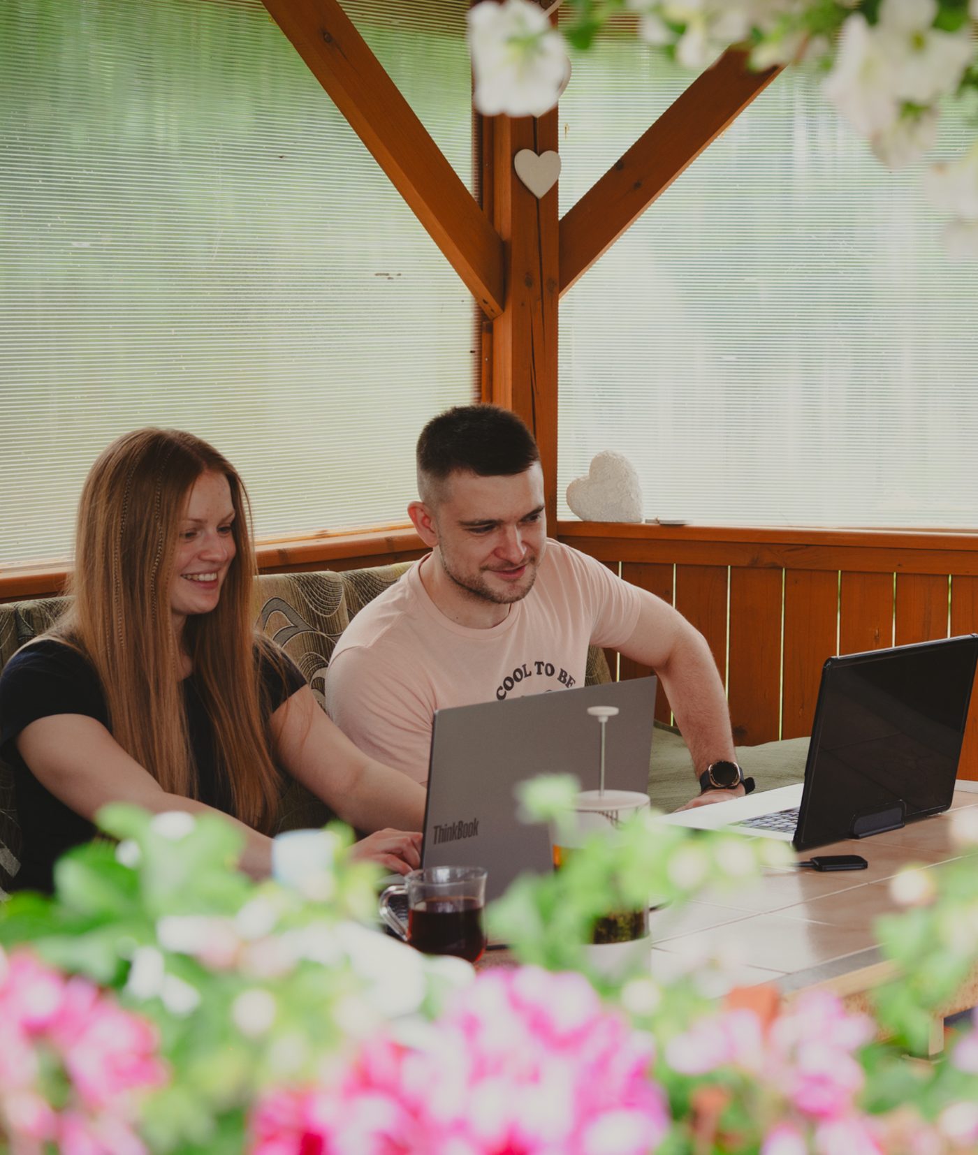 Para pracująca przy laptopach w altanie otoczonej zielenią i kwiatami
